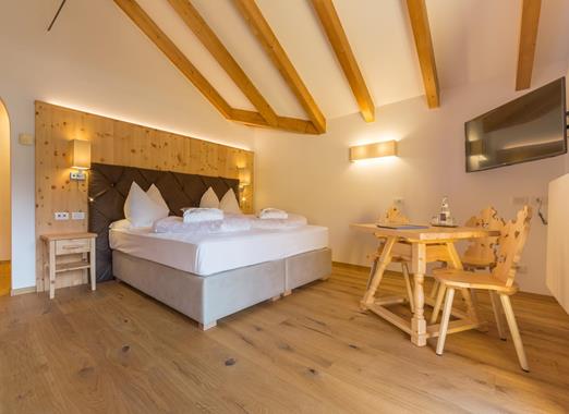 Bedroom of the Natura Suite at Hotel Villa Stefania with double bed, exposed wooden beams, and a wooden table and chairs.
