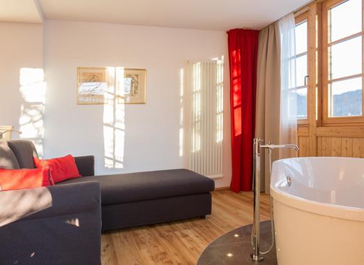 Romantic Suite at Hotel Villa Stefania with freestanding bathtub, cosy seating area and elegant wooden furnishings.