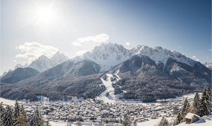 San Candido in winter with snow-covered rooftops, trees and mountains in the background.