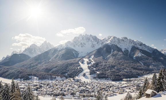San Candido in winter with snow-covered rooftops, trees and mountains in the background.