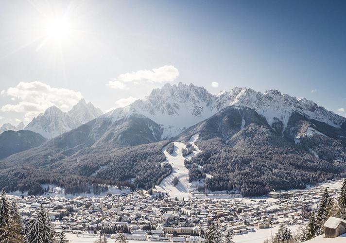 San Candido in winter with snow-covered rooftops, trees and mountains in the background.