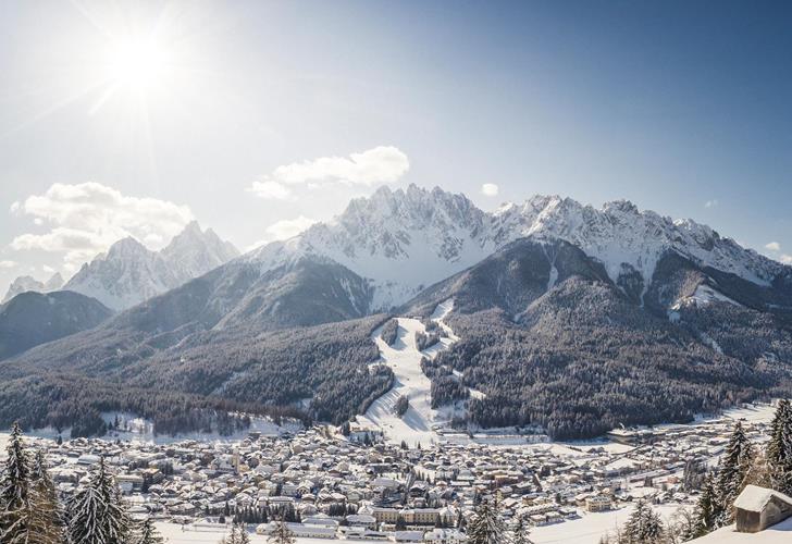 San Candido in winter with snow-covered rooftops, trees and mountains in the background.