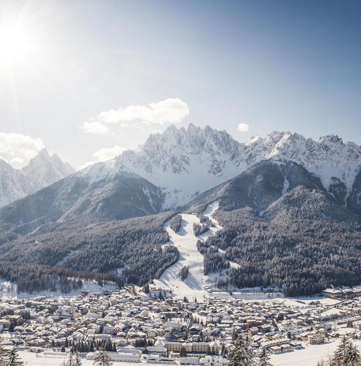 nnichen im Winter mit verschneiten Dächern, Bäumen und Bergen im Hintergrund.