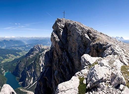 Croda del Becco rocciosa con croce di vetta e vista sul paesaggio alpino circostante.