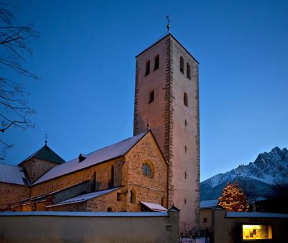 The church of San Candido in the evening light, with snow-covered mountains in the background.