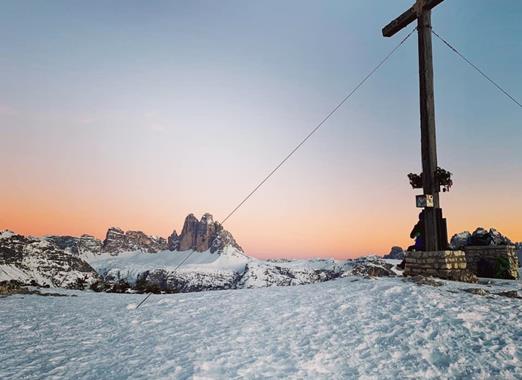 Croce di vetta sul Monte Specie al tramonto in inverno, con montagne innevate sullo sfondo.