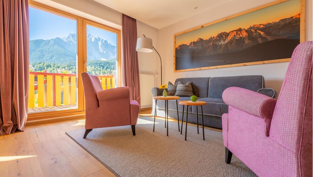 Suite Dolomiti con angolo soggiorno, poltrone e tavolini davanti a un’ampia vetrata con vista sulle Dolomiti.