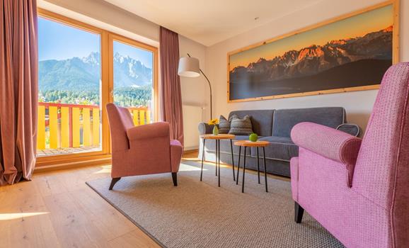 Suite Dolomiti mit Sitzecke, Sesseln und kleinen Tischen vor großer Fensterfront mit Blick auf die Dolomiten.