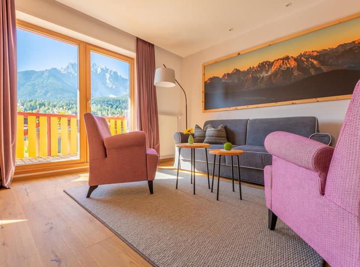 Suite Dolomiti con angolo soggiorno, poltrone e tavolini davanti a un’ampia vetrata con vista sulle Dolomiti.