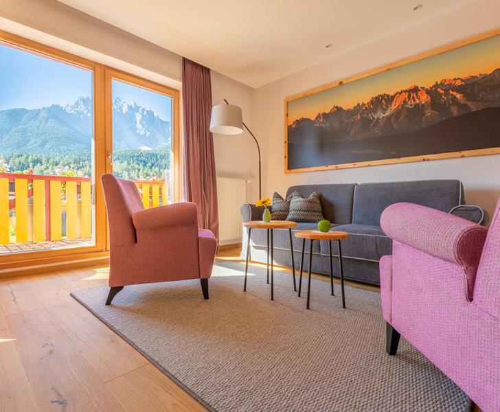 Suite Dolomiti mit Sitzecke, Sesseln und kleinen Tischen vor großer Fensterfront mit Blick auf die Dolomiten.