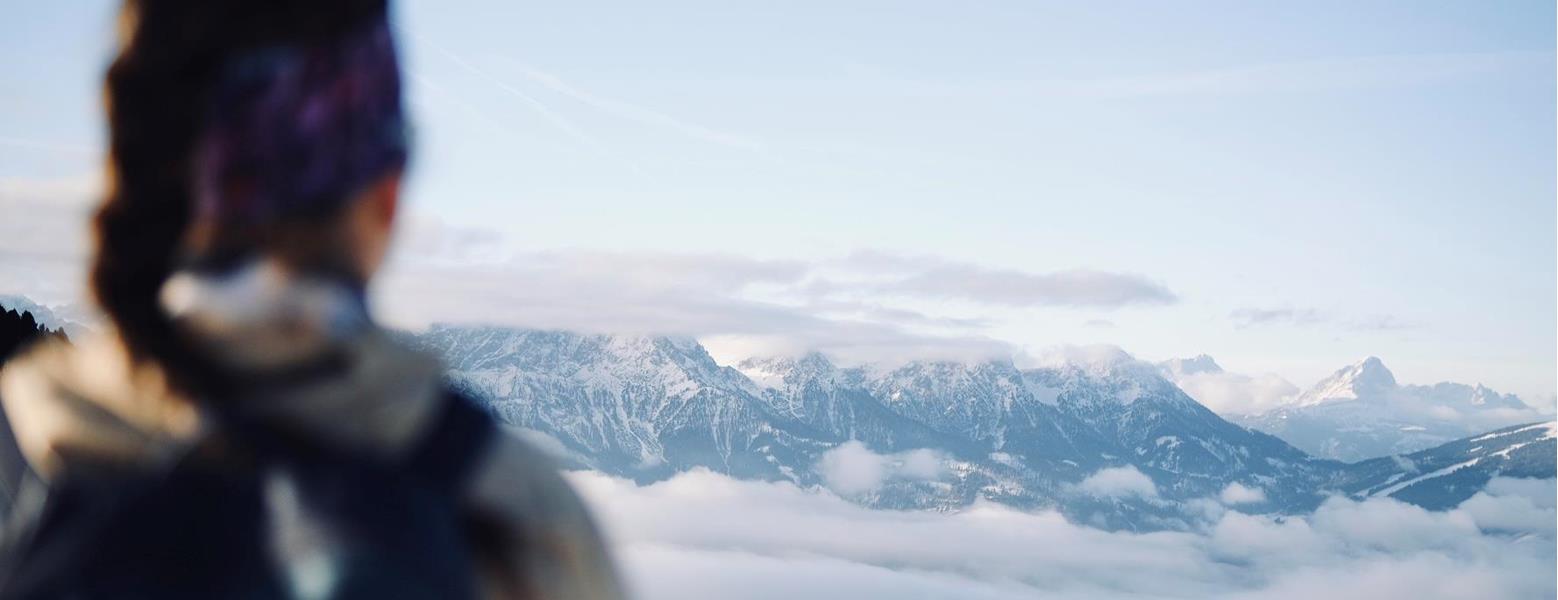 Hiker looking out over a sea of clouds and the mountain landscape of the Dolomites from a viewpoint.
