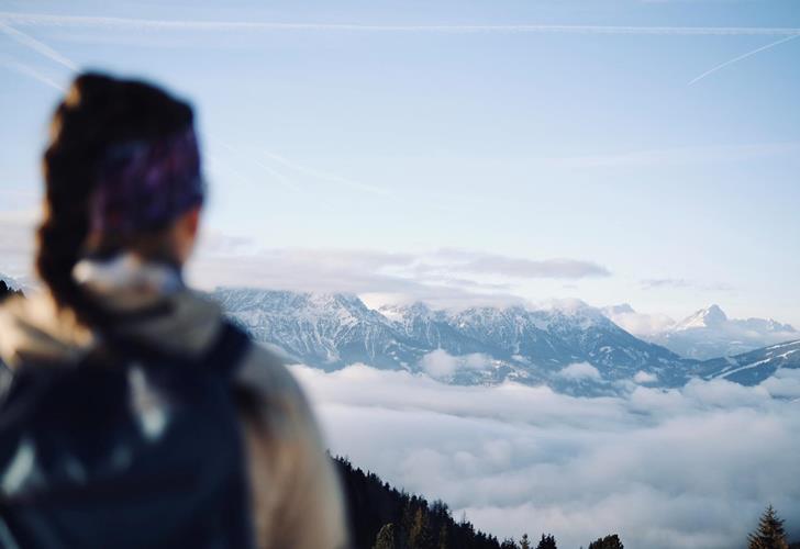 Hiker looking out over a sea of clouds and the mountain landscape of the Dolomites from a viewpoint.