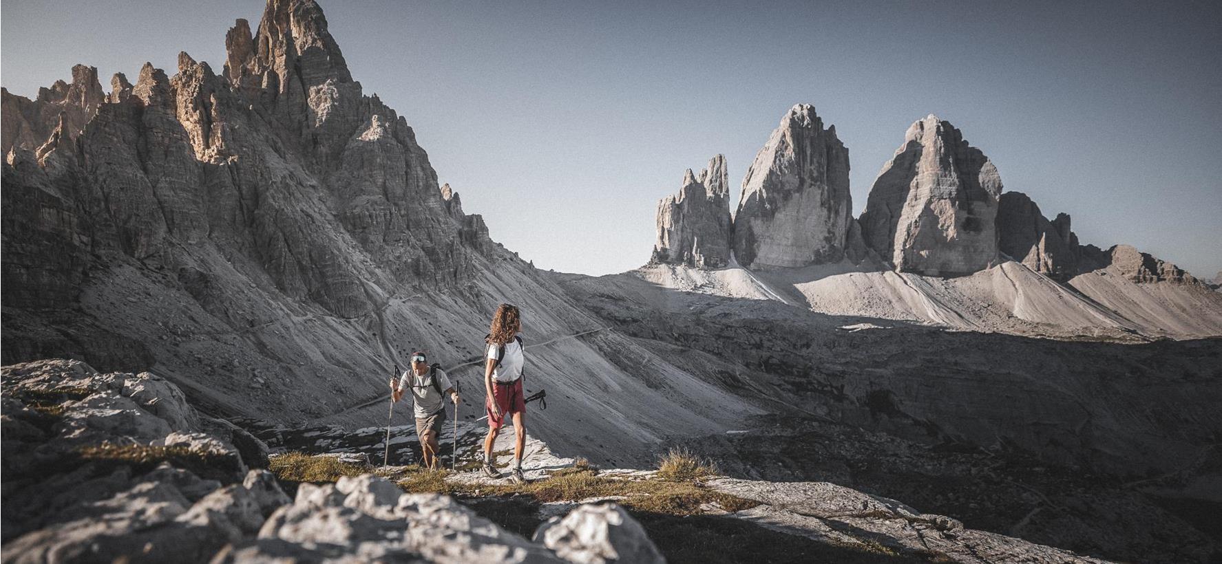 Due escursionisti su un sentiero roccioso immerso nell’imponente paesaggio dolomitico dell’area delle Tre Cime di Lavaredo.