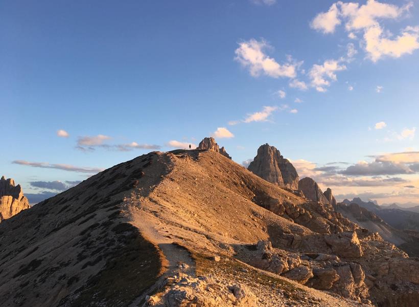 Wanderer auf einem Berggipfel in den Dolomiten mit Blick auf die imposante Berglandschaft und den weiten Himmel.