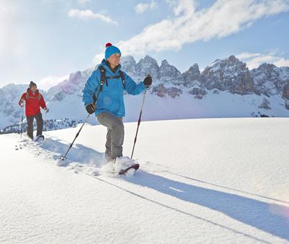 Snowshoe hiker in a snow-covered landscape, with the Dolomites in the background.