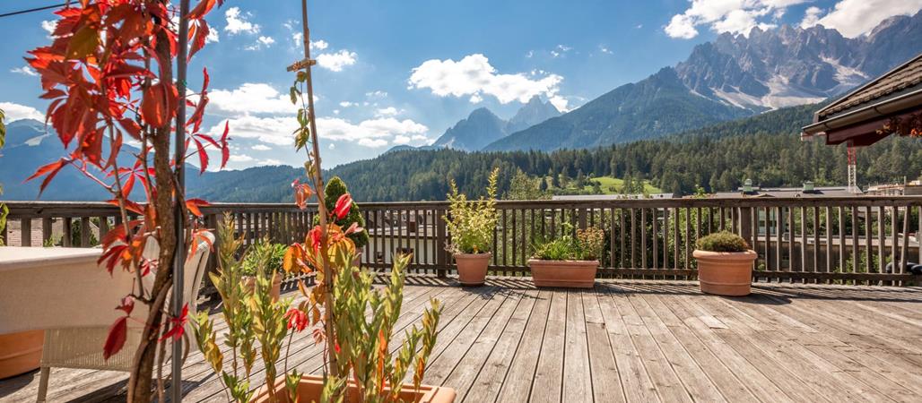 Terrazza della Suite Panorama con piante autunnali e vista sulle Dolomiti circostanti illuminate dal sole.