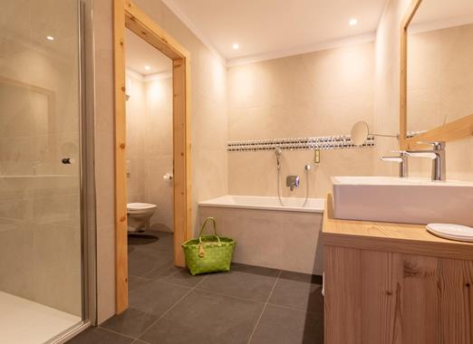 Badezimmer der Suite Dolomiti im Hotel Villa Stefania mit Badewanne, Doppelwaschbecken und eleganter Holzeinrichtung.