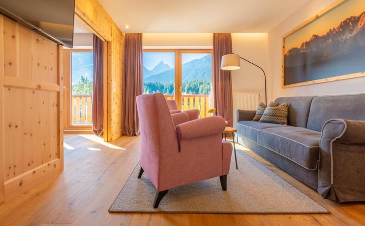 Suite Dolomiti mit Sitzecke, Sesseln und kleinen Tischen vor großer Fensterfront mit Blick auf die Dolomiten.