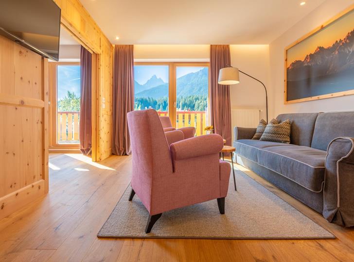 Suite Dolomiti con angolo soggiorno, poltrone e tavolini davanti a un’ampia vetrata con vista sulle Dolomiti.