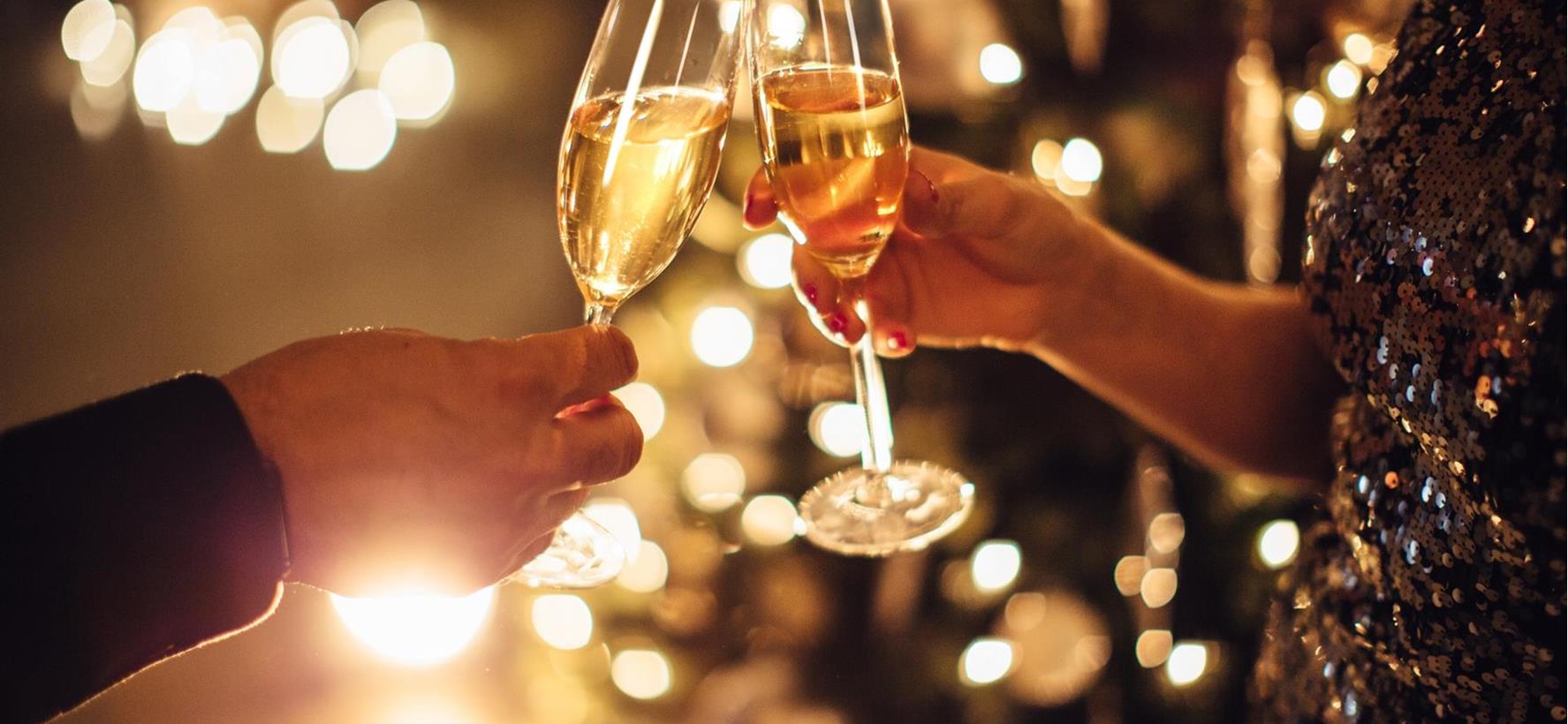 Due persone brindano con calici di spumante davanti a uno sfondo festosamente illuminato.