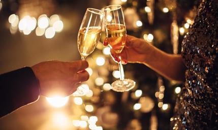 Due persone brindano con calici di spumante davanti a uno sfondo festosamente illuminato.