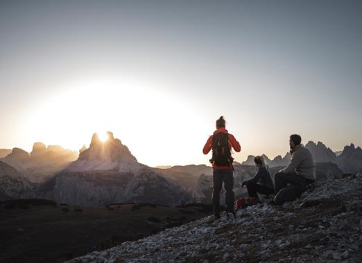 Escursionista su una montagna all’alba con un’imponente panorama montano sullo sfondo.