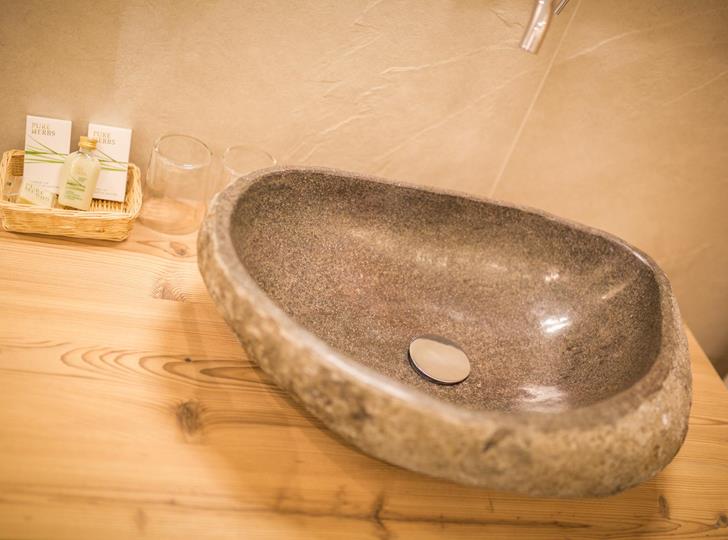 Naturstein-Waschbecken auf einer Holzplatte mit warmer Beleuchtung und natürlichen Materialien.
