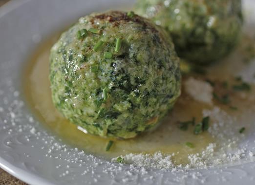 Spinatknödel auf einem weißen Teller mit geschmolzener Butter und Parmesankäse.