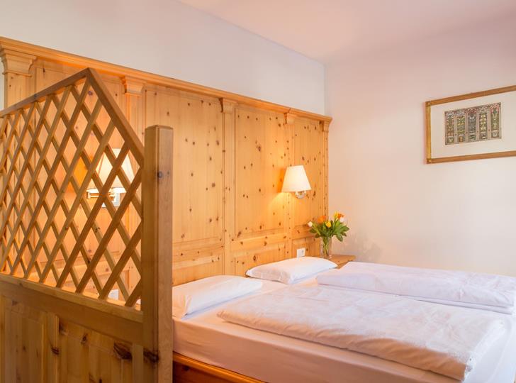 Zimmer Superior mit Doppelbett, heller Holzvertäfelung und Holztrennwand.