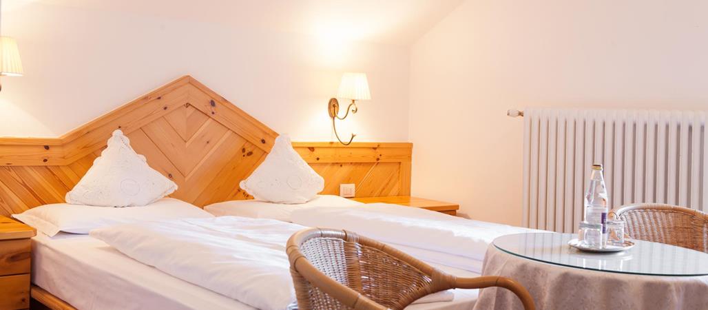 Classic double room with a wooden bed, white linens, sloped ceiling and a seating area with two chairs and a round table.