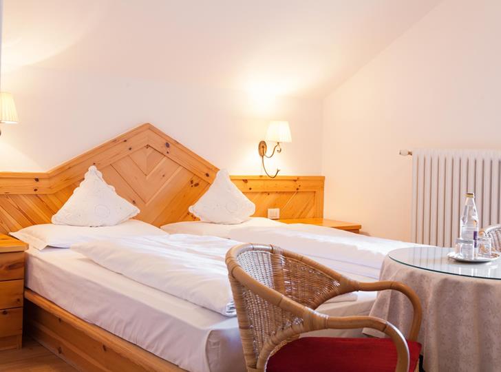 Doppelzimmer Classic mit Holzbett, weißer Bettwäsche, Dachschräge und Sitzecke mit zwei Stühlen und rundem Tisch.
