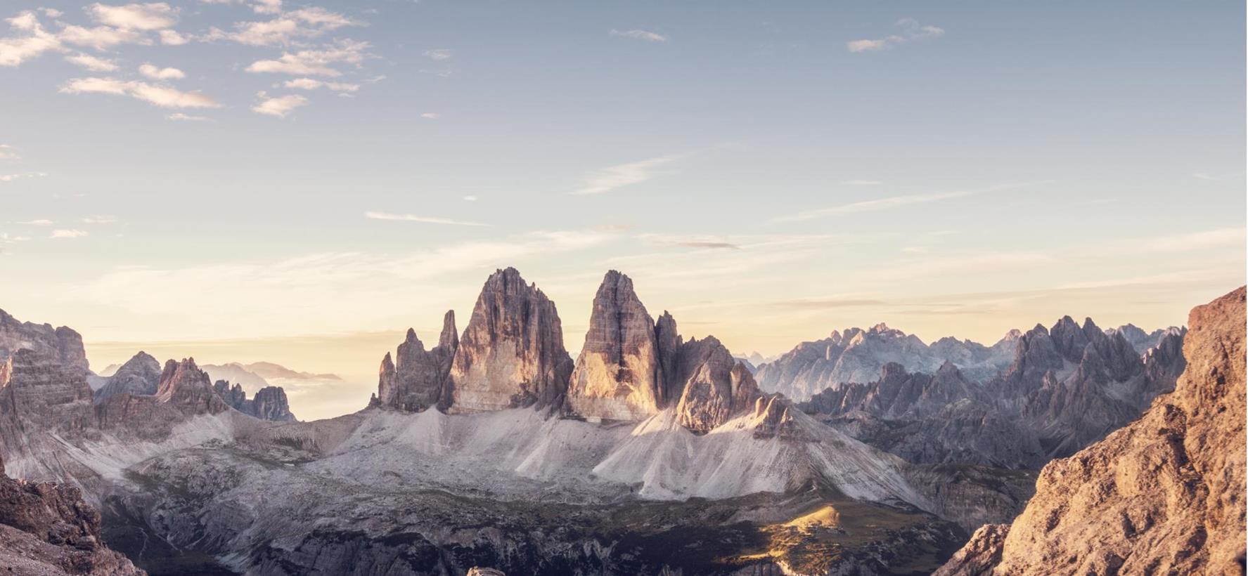 Panoramablick auf die Drei Zinnen in den Dolomiten umgeben von alpiner Landschaft und weichem Licht am Morgenhimmel.