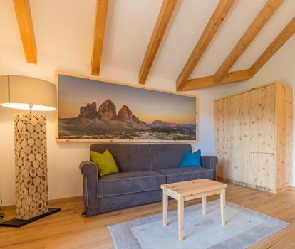 Wohnbereich der Suite Natura im Hotel Villa Stefania mit grauem Sofa, bunten Kissen, Couchtisch und Holzbalken an der Decke.