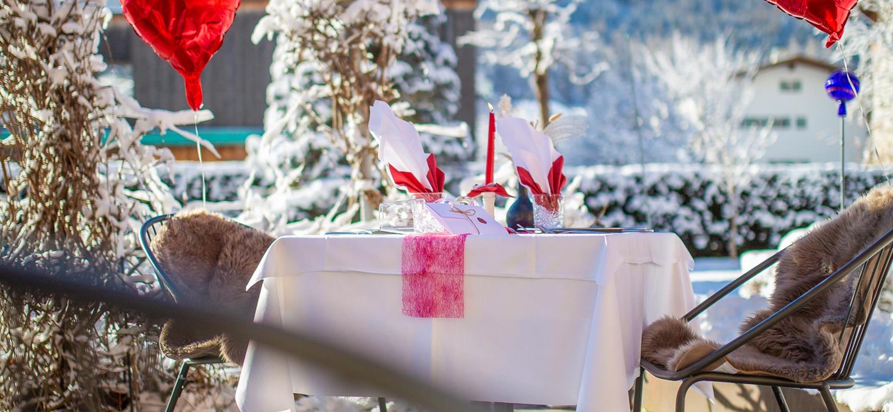 Romantically set table with red heart-shaped balloons in the snow-covered garden of Villa Stefania, with the Dolomite peaks in the background.