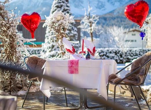 Romantisch gedeckter Tisch mit roten Herzballons im verschneiten Garten der Villa Stefania und Dolomitengipfeln im Hintergrund.