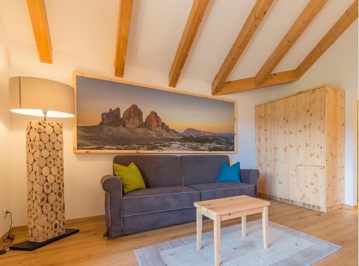 Wohnbereich der Suite Natura mit Sofa, kleinem Tisch, Stehlampe und sichtbaren Holzbalken.
