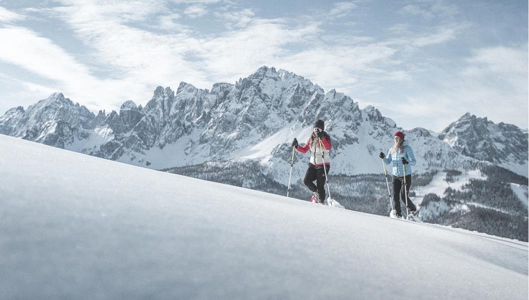 Snowshoe hikers in a snow-covered landscape with the impressive Dolomites in the background.
