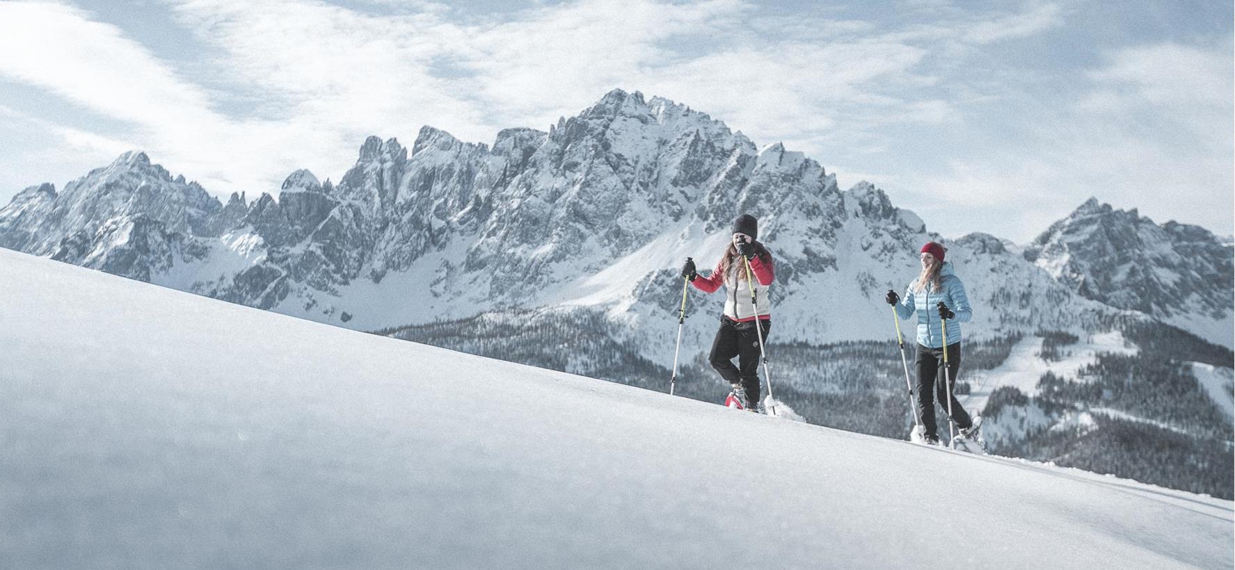 Schneeschuhwanderer in schneebedeckter Landschaft mit den markanten Dolomiten im Hintergrund.
