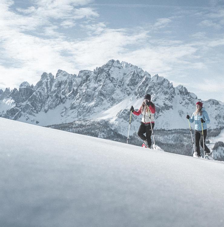 Snowshoe hikers in a snow-covered landscape with the impressive Dolomites in the background.