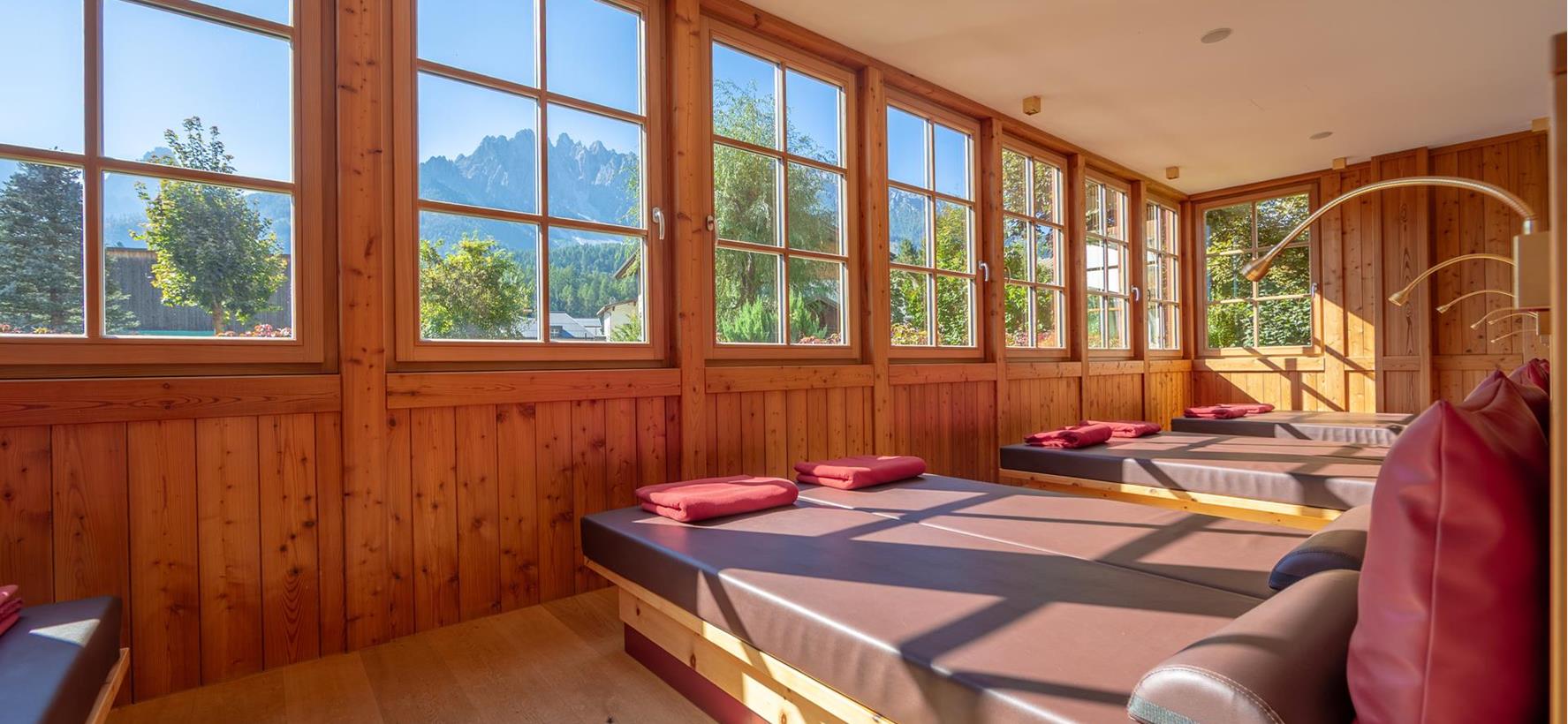 Ruheraum mit Liegen, Holzwänden und Panoramafenstern mit Blick auf die Berglandschaft.