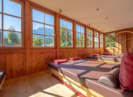 Ruheraum mit Liegen, Holzwänden und Panoramafenstern mit Blick auf die Berglandschaft.