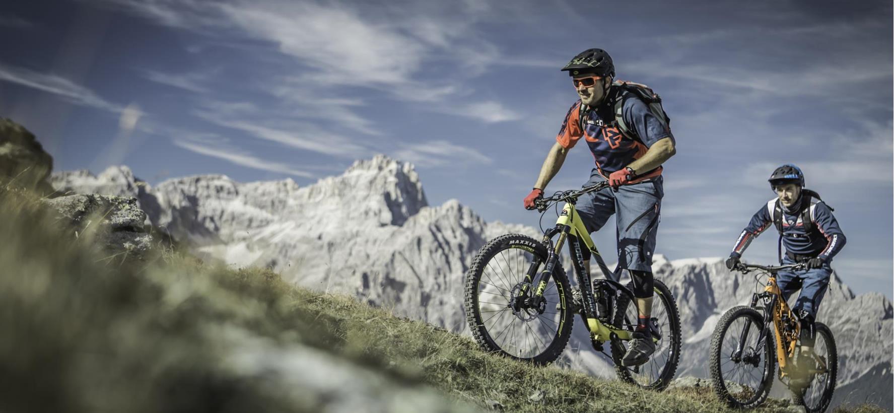 Two mountain bikers on a trail through the summer mountain landscape of the Dolomites
