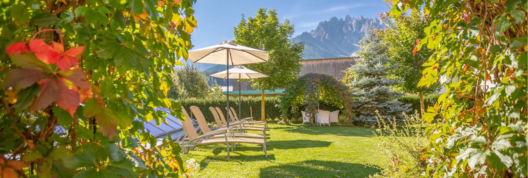 Giardino di Villa Stefania con lettini, ombrelloni e vista sulle Dolomiti circostanti.