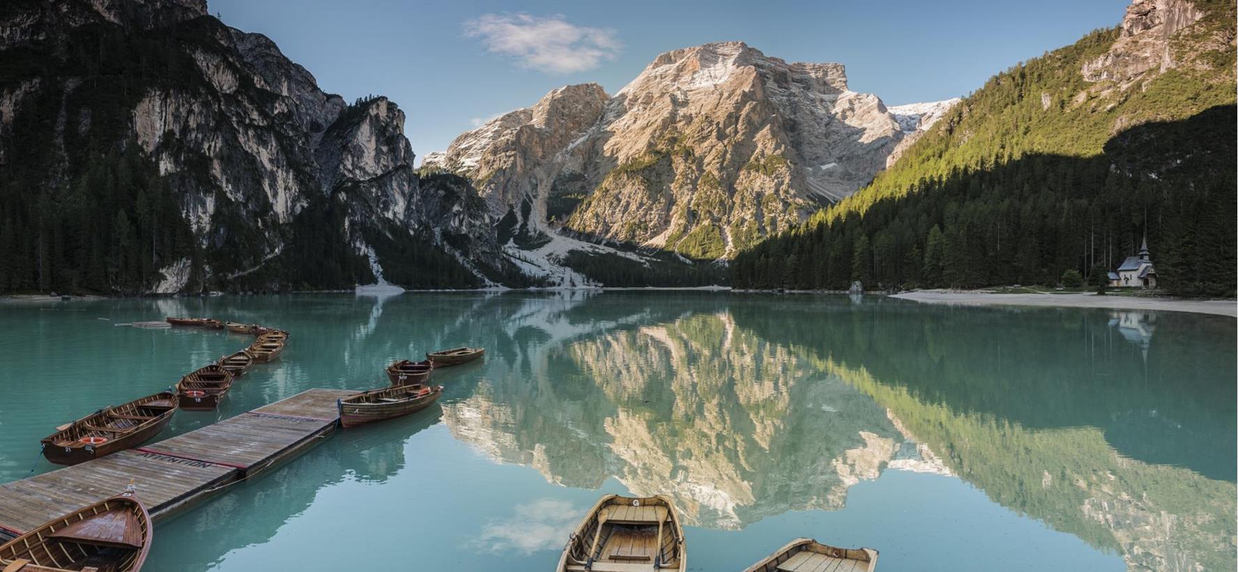 Lake Braies in summer with boats in the foreground, forests and mountains in the background.