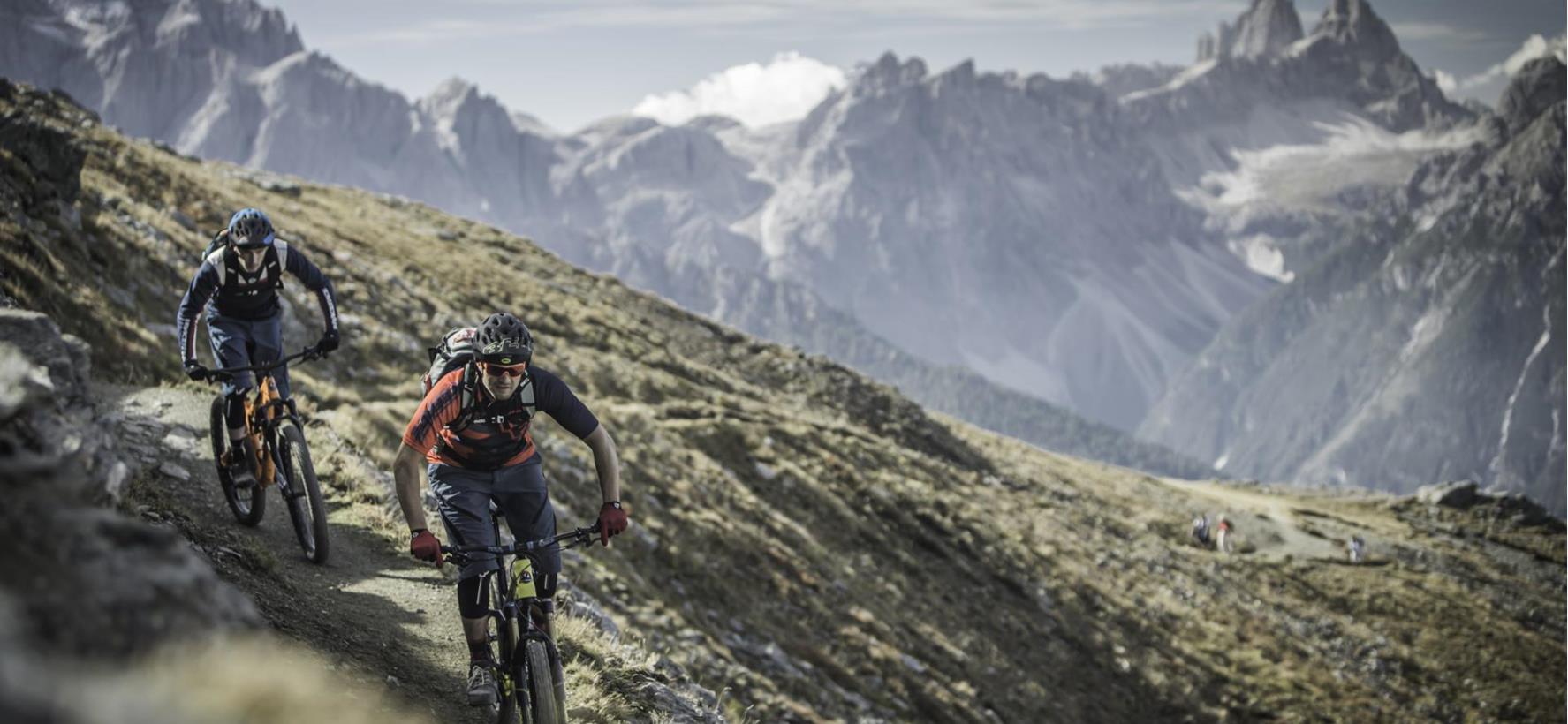 Two mountain bikers on a trail through the summer mountain landscape of the Dolomites