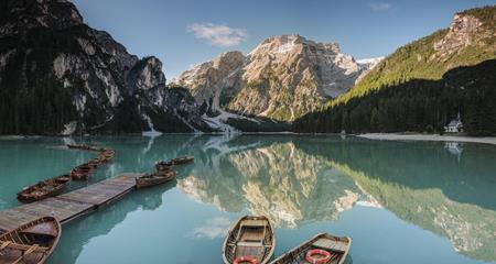 Pragser Wildsee im Sommer mit Booten im Vordergrund, Wäldern und Bergen im Hintergrund.