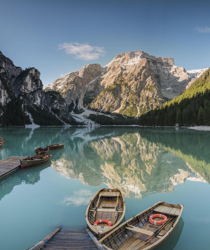 Pragser Wildsee im Sommer mit Booten im Vordergrund, Wäldern und Bergen im Hintergrund.