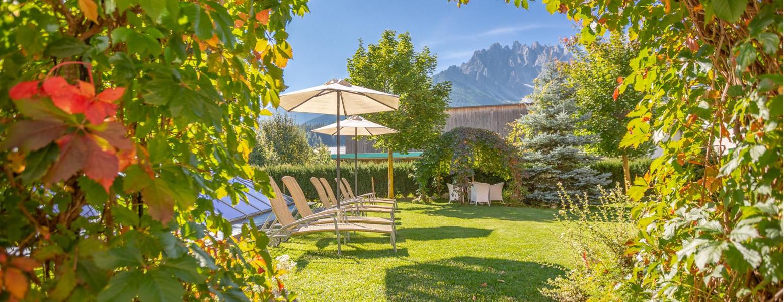 Garten der Villa Stefania mit Liegestühlen, Sonnenschirmen und den Dolomiten im Hintergrund.