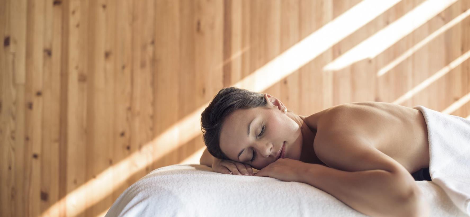A woman is lying relaxed on a massage table in a sunlit room.