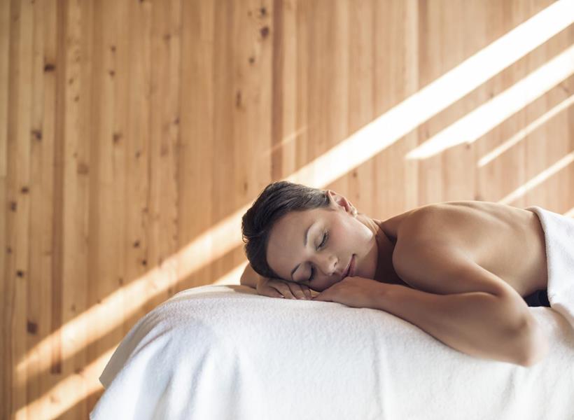 Eine Frau liegt entspannt auf einer Massageliege in einem Sonnendurchfluteten Raum.